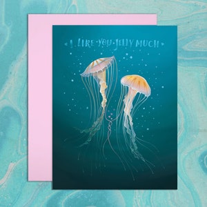 Blue, watery background. Illustration of two colorful sea nettle jellyfish with long swirling tentacles. Two of their tentacles are entwined among small, pink, heart shaped bubbles. Hand drawn text in watery font says, I Like You Jelly Much