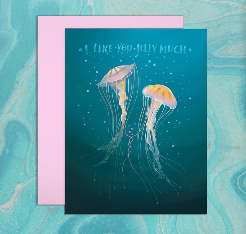 Blue, watery background. Illustration of two colorful sea nettle jellyfish with long swirling tentacles. Two of their tentacles are entwined among small, pink, heart shaped bubbles. Hand drawn text in watery font says, I Like You Jelly Much