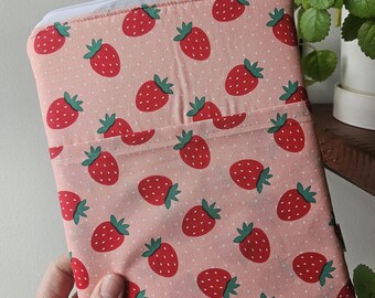 Pode incluir: Uma bolsa rosa com zíper com um padrão repetido de morangos vermelhos com caules verdes e bolinhas brancas. A bolsa tem um zíper branco e um pequeno bolso na frente.