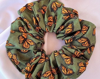 Może przedstawiać: Zielona scrunchie z nadrukiem motyli. Motyle są pomarańczowe z czarnymi oznaczeniami.