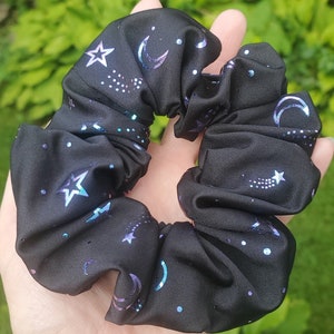 May include: Black scrunchie with a celestial print featuring silver stars, moons, and shooting stars on a black background.