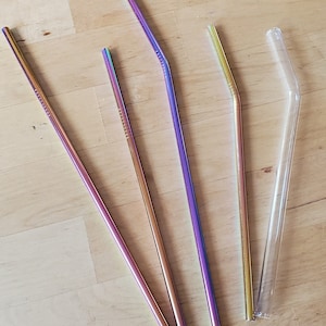 May include: Four drinking straws, three are metal and iridescent with a rainbow sheen, one is clear glass. All are bent.
