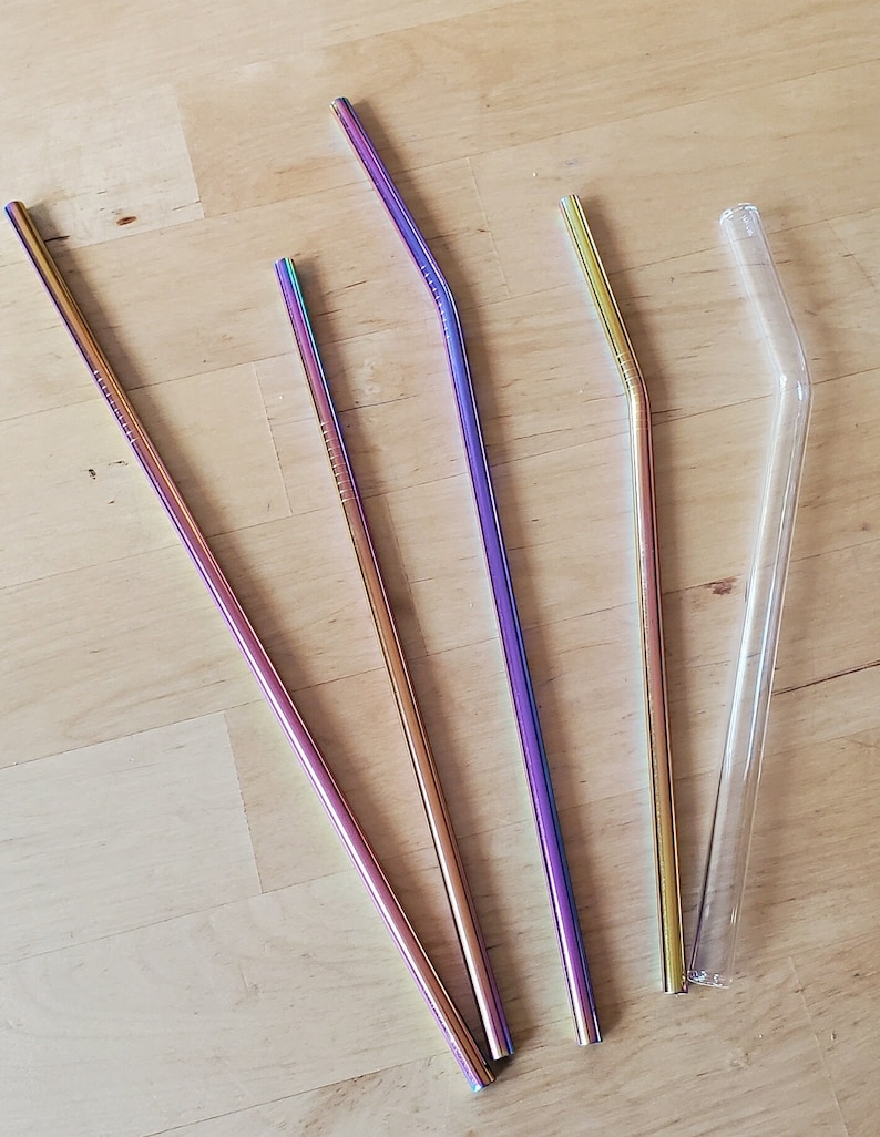 May include: Four drinking straws, three are metal and iridescent with a rainbow sheen, one is clear glass. All are bent.