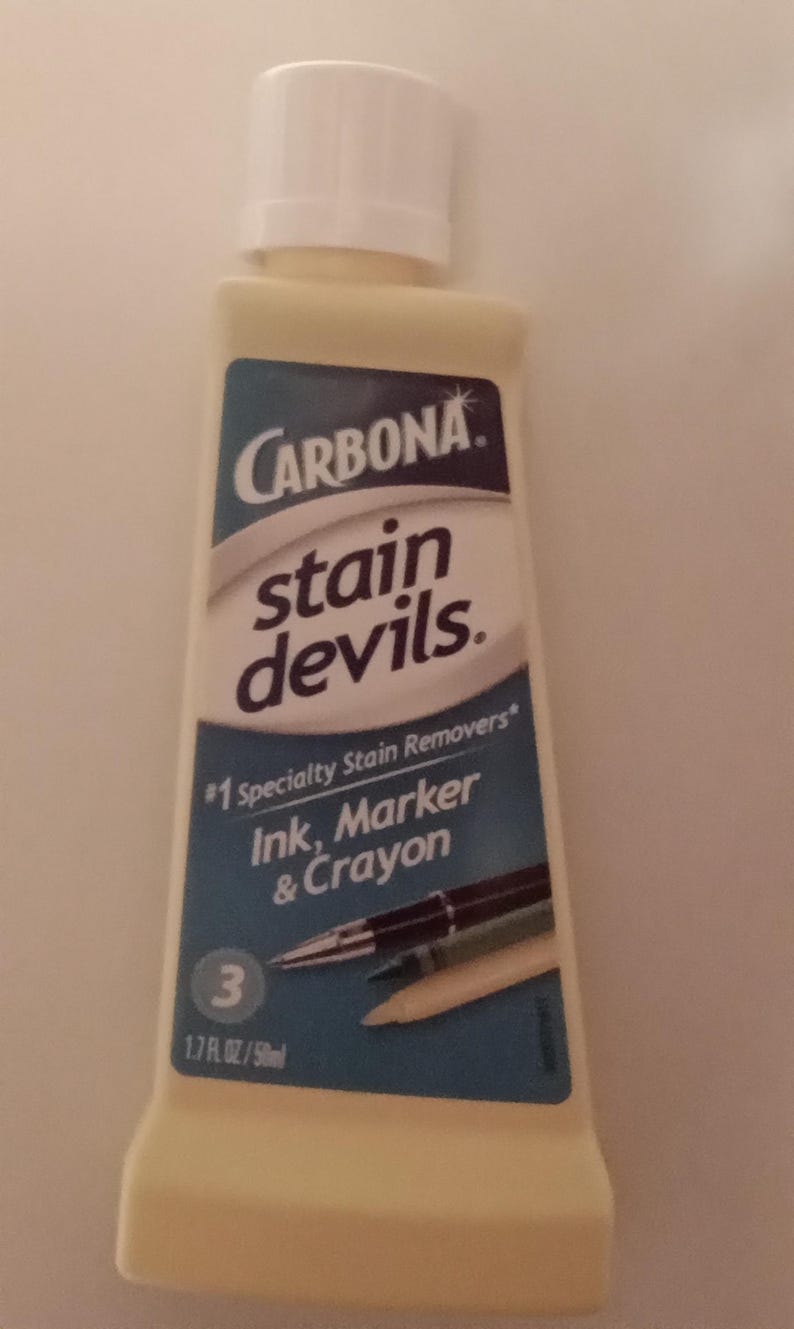 K&ouml;nnte beinhalten: Eine Flasche Carbona Stain Devils Fleckenentferner f&uuml;r Tinten-, Marker- und Buntstiftflecken. Die Flasche ist hellgelb mit wei&szlig;em Deckel und blauem Etikett mit Produktname und einer Grafik von Stiften und Bleistiften. Enth&auml;lt 50ml.