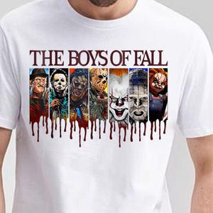 May include: A white t-shirt featuring the text THE BOYS OF FALL in dark red letters above seven vertical panels depicting various horror movie characters. Below the panels, a dark red graphic effect resembles dripping blood across the chest.