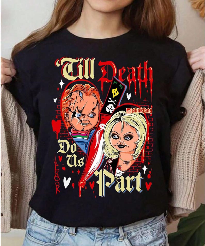 May include: A black t-shirt featuring a graphic print of two horror movie dolls, Chucky and Tiffany, separated by a large knife. The text Till Death Do Us Part is printed in a stylized font, accompanied by red hearts, blood drips, and a brick wall background.