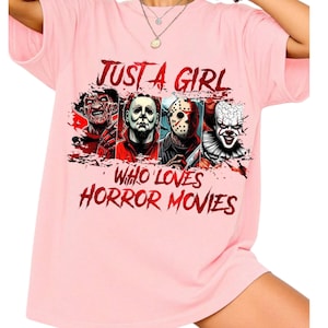 May include: A light pink short-sleeved t-shirt featuring a graphic print of four horror movie characters. The text reads JUST A GIRL WHO LOVES HORROR MOVIES in a distressed red font. The characters include Freddy Krueger, Michael Myers, Jason Voorhees, and Pennywise.