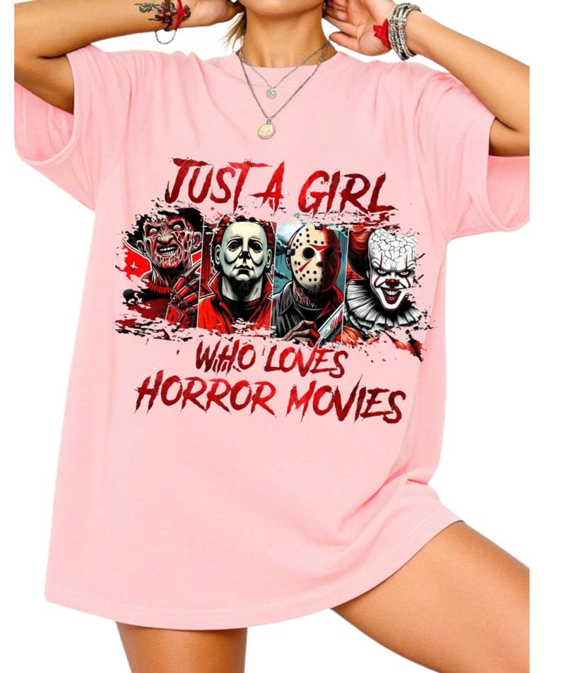 May include: A light pink short-sleeved t-shirt featuring a graphic print of four horror movie characters. The text reads JUST A GIRL WHO LOVES HORROR MOVIES in a distressed red font. The characters include Freddy Krueger, Michael Myers, Jason Voorhees, and Pennywise.