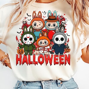 May include: A cream-colored t-shirt featuring a graphic print of five cartoon characters dressed in Halloween costumes, including masks and props, with the word HALLOWEEN in red, dripping, blood-like lettering at the bottom of the design.