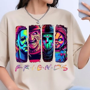 May include: A beige short-sleeved t-shirt featuring a graphic print of four horror movie characters in vibrant neon colors. Below the characters, the word "F.R.I.E.N.D.S" is printed in a colorful, multi-toned font across the chest area.