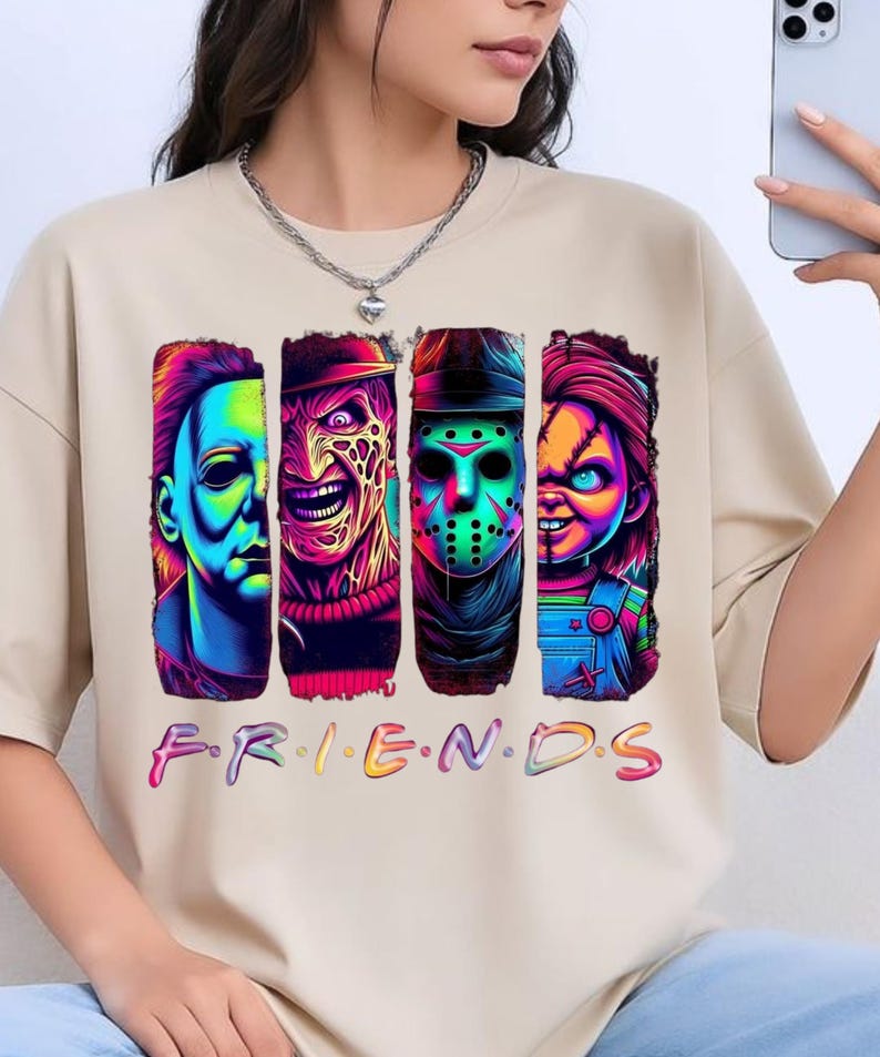 May include: A beige short-sleeved t-shirt featuring a graphic print of four horror movie characters in vibrant neon colors. Below the characters, the word "F.R.I.E.N.D.S" is printed in a colorful, multi-toned font across the chest area.