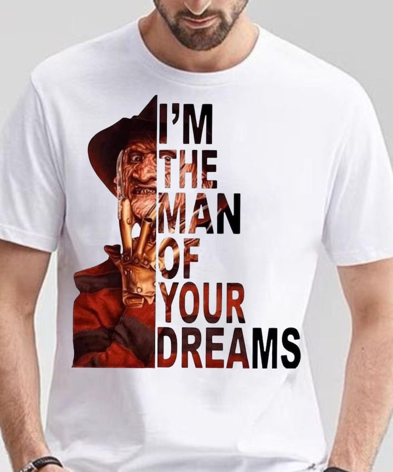 May include: A white short-sleeved t-shirt featuring a graphic of a character wearing a brown hat and a red and black striped sweater, with a clawed hand near the face. The text "I'M THE MAN OF YOUR DREAMS" is printed in black capital letters.