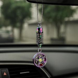 Puede incluir: Un accesorio para coche con un resorte de color arcoíris y un dije de rueda. El dije cuelga de una cadena plateada, diseñado para colgar del espejo retrovisor. La rueda tiene un diseño en forma de estrella con un centro amarillo.
