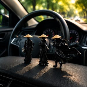 May include: Three black samurai figurines with straw hats are displayed on a car dashboard. The figurines are in different poses, one holding a sword, another with crossed arms, and the third with a flowing cape. The background includes a steering wheel and a blurred view of a road.