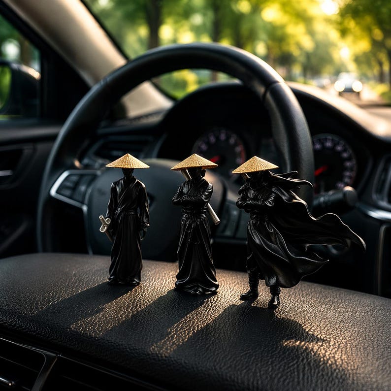May include: Three black samurai figurines with straw hats are displayed on a car dashboard. The figurines are in different poses, one holding a sword, another with crossed arms, and the third with a flowing cape. The background includes a steering wheel and a blurred view of a road.
