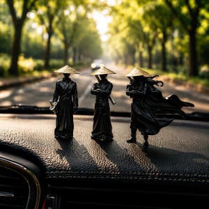 May include: Three black samurai figurines with gold-colored hats and swords are displayed on a car dashboard. The figurines are in various poses, with one holding a sword, another with crossed arms, and the third with a flowing cape.