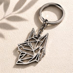 Op de afbeelding: Een zilverkleurige sleutelhanger met een geometrisch wolfskopontwerp. De sleutelhanger heeft een splitring en een ketting die verbonden is met de wolfskop hanger. De hanger is gemaakt van metaal.
