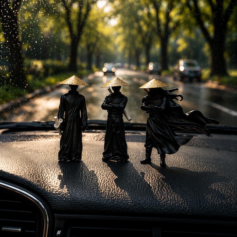 May include: Three black figurines of samurai warriors wearing conical straw hats with gold trim. The figures are posed on a dark surface, with a blurred road and trees in the background. The figures are in various stances, some holding weapons.