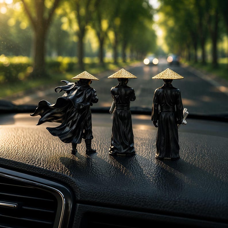 May include: Three miniature figurines of Asian warriors in black attire and straw hats are displayed on a car dashboard. The figurines are facing away from the viewer, with one figure's cape billowing in the wind. The background shows a tree-lined road.