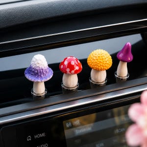 May include: Four small mushroom-shaped car air vent clips featuring distinct caps: a white-to-purple gradient textured cap, a red cap with white spots, a yellow textured cap, and a smooth purple conical cap, all with white stems.