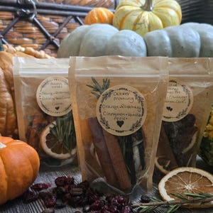 May include: Three clear stand-up pouches filled with dried orange slices, cinnamon sticks, and rosemary sprigs. Each pouch features a round beige label with the text October morning, Orange, Rosemary, Cinnamon, Vanilla, Apple, and a heart icon.