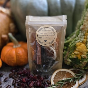 May include: A clear stand-up pouch filled with coffee beans, dried orange slices, and cinnamon sticks. A round beige label on the front reads: Autumn Coffeehouse, Coffee beans, Orange, Cinnamon, Vanilla, Apple, Cloves, with a small heart icon.