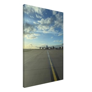 Op de afbeelding: Een canvas print van een vliegtuig op een landingsbaan, onder een blauwe lucht met pluizige witte wolken. Het vliegtuig staat in het midden, met de neus naar de kijker gericht. De landingsbaan heeft een gele middenlijn.