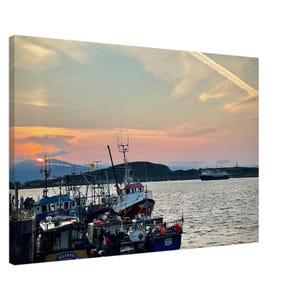 May include: A canvas print of a harbor scene at sunset. Several fishing boats are docked, with their masts and equipment silhouetted against the colorful sky. A ferry is visible in the distance, and the water reflects the warm hues of the setting sun.