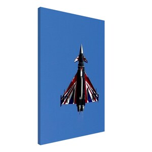 May include: A canvas print of a fighter jet against a clear blue sky. The jet features a design incorporating the Union Jack flag in red, white, and blue. The aircraft is viewed from below, showcasing its wings and tail.