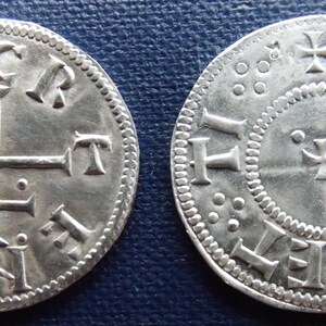 May include: Two silver coins with intricate designs. One coin features a cross and the letters "C R T I N E" around the edge. The other coin has a central cross and the letters "I H E N I" around the edge, with a dotted border.