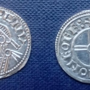 May include: Two silver coins with detailed engravings. One coin features a profile of a figure wearing a helmet and holding a staff. The other coin displays a cross within a shield design, surrounded by text.