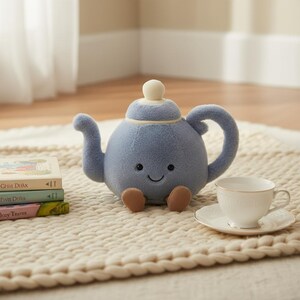 May include: A plush, light blue teapot with a smiling face, brown feet, and a white lid. A white teacup and saucer are next to the teapot. The teapot is on a cream-colored rug.