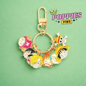 Puede incluir: Llavero dorado con múltiples dijes de caras de personajes de anime. Los dijes son coloridos y detallados, con diversas expresiones. El llavero tiene un cierre y un anillo. El texto "POPIES PINS" está en la esquina superior derecha.