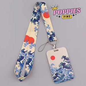 Puede incluir: Un cordón con un fondo crema con un patrón de olas azules y soles rojos. El portatarjetas a juego tiene el mismo diseño. El cordón tiene un cierre de metal y una cuerda negra.