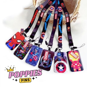 Puede incluir: Una colección de cordones y tarjeteros con temática de Marvel. Los cordones son negros con nombres y logotipos de personajes, incluyendo Spider-Man y Capitán América. Los tarjeteros presentan varios personajes de Marvel y la palabra "Marvel". La imagen también incluye el texto "POPPIES PINS".