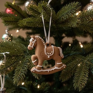 May include: A brown rocking horse ornament with white icing-style detailing on the mane, saddle, and rockers. The horse is suspended by a thin white ribbon, featuring a textured surface that mimics the appearance of a baked gingerbread cookie.