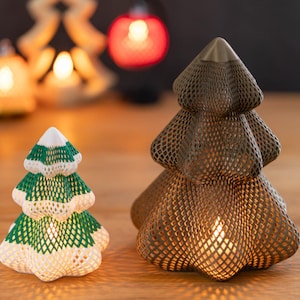 May include: Two decorative tree-shaped lanterns with a lattice structure. The smaller tree is white with green accents, while the larger tree is a solid dark brown. Both feature a hollow interior that emits a warm light from within.