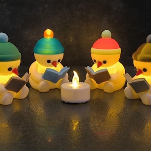 May include: Four yellow, snowman-like figures with orange carrot noses, each wearing a different coloured beanie cap and holding a small book. They are arranged in a circle around a central white, battery-operated tea light with a flickering flame.