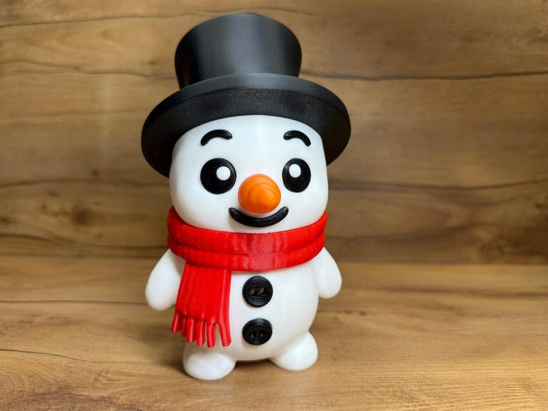 May include: A white snowman figurine featuring a black top hat, a bright orange carrot-shaped nose, and a red scarf wrapped around its neck. The snowman has two black circular buttons on its torso, black eyes, and a black curved mouth.