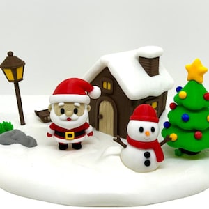 May include: A miniature Christmas scene featuring a Santa Claus figure, a snowman with a red scarf, a brown house with a white snow-covered roof, a green Christmas tree with colourful ornaments and a yellow star, and a brown street lamp.