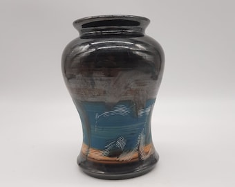 May include: A small, black ceramic vase with a blue and orange glaze. The vase has a wide mouth and a narrow base.