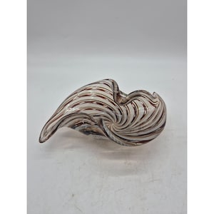 May include: A decorative glass bowl with a swirling design. The bowl features alternating bands of brown, white, and clear glass, creating a spiral effect. The bowl has an organic, asymmetrical shape, with a wide opening and a pointed end.