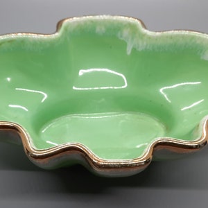 May include: A green ceramic bowl with a gold rim. The bowl has a wavy edge and a smooth, glossy finish.