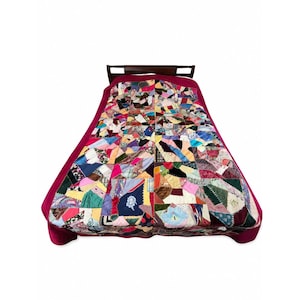 May include: A patchwork quilt featuring a variety of multi-colored fabric scraps in diverse patterns and textures, including floral, plaid, and solid prints. The quilt is bordered by a solid magenta fabric and draped over a dark wooden headboard.