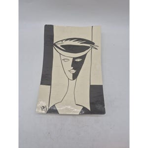 May include: Rectangular ceramic plate with a stylized black and white illustration of a woman's face wearing a hat with a fish on it. The plate has a cream-colored background with black geometric shapes. The artist's signature is in the lower left corner.