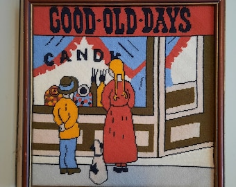 May include: A framed needlepoint picture of a storefront with the words "GOOD-OLD-DAYS" above the window. The window says "CANDY" and depicts two people and a dog in front of the store.