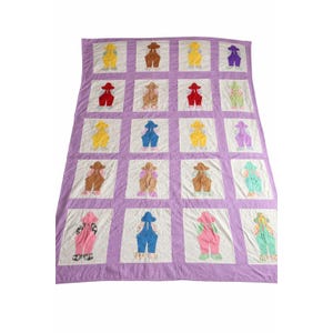 May include: A handmade quilt with a lavender border and white squares. Each square features a colorful applique of overalls in various colors, including yellow, red, brown, blue, pink, and green. The quilt is a patchwork design.