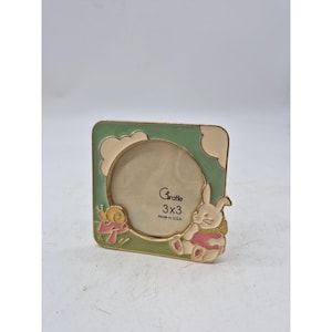 May include: A square photo frame with a green and beige border, featuring a cartoon bunny and snail. The frame is designed for a 3x3 inch photo and has the text "Graffe 3x3 Made in USA".