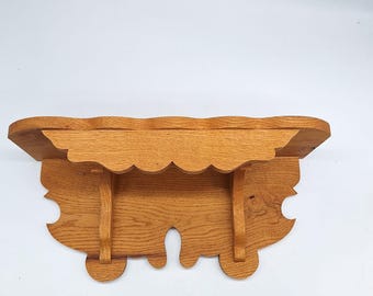May include: A wooden shelf with a scalloped edge and intricate carvings. The shelf is made of light brown wood and has a rustic appearance.