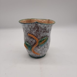 May include: A small, white ceramic vase with a speckled glaze. The vase has a scalloped rim and is decorated with a green and orange leaf design.